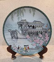 Full view of the vintage Chinese porcelain plate on a stand showing garden scene, architecture, floral elements, people, and calligraphy.