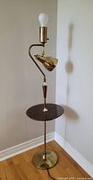 Full view of vintage floor lamp showing brass finish, wood table surface, and bulb socket on top.