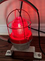 Front view of the vintage industrial red lantern illuminated and showing the ribbed glass lens and red protective cage.