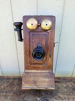 Front view of antique wooden wall telephone showing brass bells and black mouthpiece.