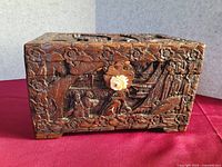 Front view of the finely hand-carved antique Chinese wooden box placed against a red cloth, showcasing detailed figures, flowers, and architectural elements.