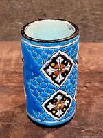 Front angle view of cylindrical porcelain vase showing bright turquoise-blue exterior glaze with repeating diamond-shaped decorative motifs and scallop patterned background.