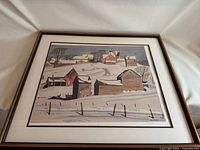 Framed print featuring a snowy winter village scene with multiple buildings and trees, signed by AJ Casson, with visible edition number 3/150.