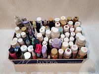 Photo showing a large box filled with various sized bottles and tubes of artist paints arranged closely together.