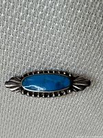Front view of Native American style brooch with oval turquoise set in the center and silver detailing.