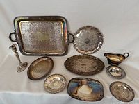 Full view of all silver plated items arranged on a white surface showing variety of trays, dishes, candlestick holder, and gravy boat.