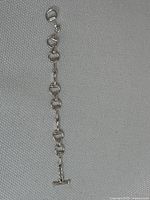 Full length view of sterling silver linked bracelet on gray woven fabric background, showing toggle clasp and link design.