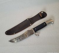 Complete view of vintage fixed blade fishing cutter with black textured handle and brown leather sheath.