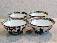 Front view of four Chinese porcelain bowls decorated with colorful rooster motifs and floral border pattern with gold trim.