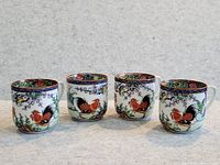 Four porcelain cups with colorful rooster and floral motifs, displayed side by side.