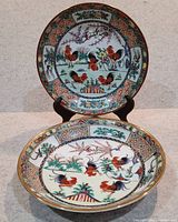Two large porcelain soup bowls with colorful rooster and floral designs, displayed upright and front facing.