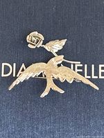 Photo of sterling silver peace themed brooch showing bird in flight with rose and leaf in beak on a dark background