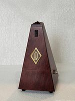 Front view of the pyramid-shaped wooden metronome with the gold diamond emblem visible.