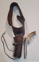 Full view of the dark brown leather western belt with embossed holster, strap, and metal toy revolver.
