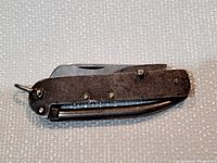 Closed view of the folding military cutter knife showing patina on metal handle and attachments.