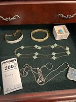 Photo showing turquoise earrings, turquoise clover-shaped stone necklace and bracelet, rhinestone bracelet, silver chain necklace with pendant, and turquoise stone ring in a box.