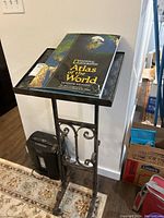Full view of metal book stand with atlas on top, showing overall condition and structure.