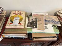 Worn hardcover and softcover books stacked on table with visible titles 'In the Winner’s Circle' and 'The Drawings of Raphael'
