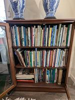 Wooden book cabinet with two upper shelves filled with assorted books and two blue and white porcelain vases on top