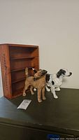 Two cast iron dog figurines in front of a wooden wine box with interior shelves and a drawer.