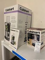Boxes and manuals of Cuisinart food processors arranged on a shelf, showing product branding and style.