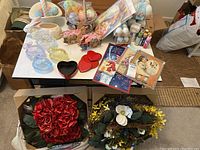 Table with various Easter ceramic, glass, plastic items, craft supplies, and floral wreaths below.