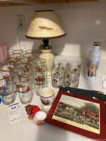 Overview of the lot items including foxhunt-themed glasses, ceramic fox figurine, egg cup, lamp, metal water bottle with fox design, and a trivet with a foxhunt painting.