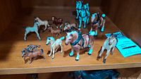 Shelf with multiple small horse figurines of various colors and details including saddles and harnesses