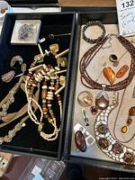 Two trays showing assorted jewelry in brown and beige tones including bead necklaces, bracelets, rings, and pendants
