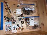 Photo of multiple pieces of beaded jewelry including Joan Rivers earrings with blue tags, multi-colored charm bracelet, large butterfly beaded earrings, and Ziploc bags with bead strands.