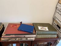 Lot overview showing red portfolio, blue book, two green books on wooden table