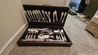 Full view of the flatware set in storage box showing forks and other pieces arranged upright in the lid area and utensils laid flat in the bottom compartment.