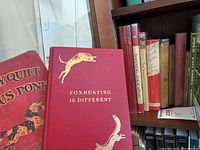 Red hardcover book 'Foxhunting is Different' on top of bookshelf with other hardback books