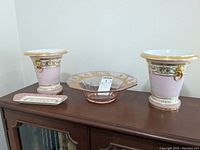 Lot arranged on wooden cabinet showing two pink planters flanking glass bowl and Spode plate