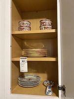 Shelf display showing two floral lidded canisters, six pink rimmed plates, four bird motif plates and spoon rest