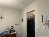 Room view showing four brass tone wall sconces mounted on white walls at various angles, each holding two green taper candles.