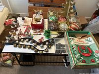 Overview of lot items including two sleigh bell straps, tree stand, box of ornaments, decorative houses, and angel figurine