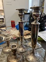 All five sterling silver candlesticks displayed on tabletop with various background items