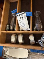 Five sterling silver napkin rings and salt and pepper shakers in a wooden drawer showing tarnish and some with mesh or perforated design