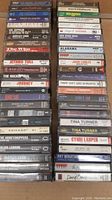 Photo showing multiple classic rock and pop cassette tapes stacked in two columns, titles visible including Bon Jovi, Led Zeppelin, Motley Crue, The Who, Jethro Tull, Journey, Tina Turner, Cyndi Lauper, David Bowie, and others.