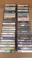 Photo showing a broad view of two stacks of assorted cassette tapes featuring popular artists from the 70s-90s pop and rock genres.