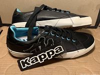 Side view of the black leather Kappa shoes with light blue inner lining, black laces, and large Kappa embroidery on the side.
