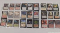 Photo showing 30 Magic The Gathering cards laid out in three rows. Includes various cards such as Plains, Mountain, and other spells and creatures.