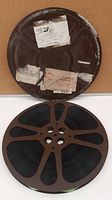 Photo of metal 16mm film reel with black film and various paper stickers on the container.