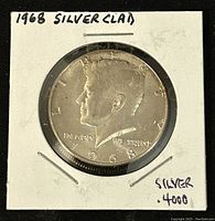 Obverse side of 1968 Kennedy Half Dollar showing John F. Kennedy profile, year 1968, and inscriptions 'LIBERTY' and 'IN GOD WE TRUST'. Coin encased in white cardboard holder.