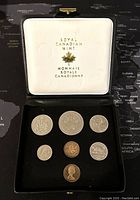 Top view of seven Canadian coins displayed in a Royal Canadian Mint case with white satin lid and black velvet base.