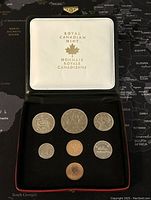 Opened black presentation case showing all 7 coins laid out in white velvet with Royal Canadian Mint logo on inside lid.