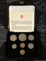 Photo showing all 7 Canadian coins from 1975 set arranged on a black velvet case along with a folded informational card about the coins.