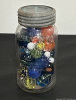 Front view of clear Crown Mason jar filled with colorful glass marbles, showing embossed lettering and metal lid