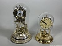 Full view of the two domed quartz mantle clocks side by side showing sizes and details under glass domes.
